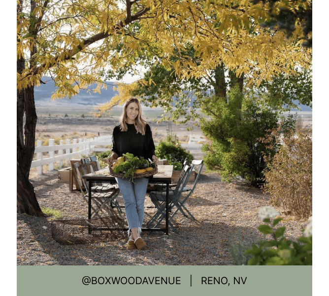 一名妇女拿着装满收获农产品的篮子，倚靠在户外餐桌上，标题写着@boxwoodavenue Reno, NV