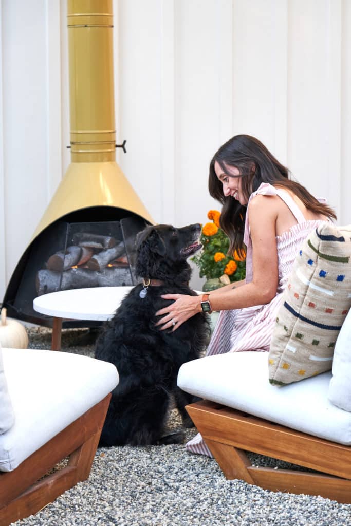 克里斯蒂和她的狗坐在户外躺椅上，旁边是他们的中世纪现代户外壁炉